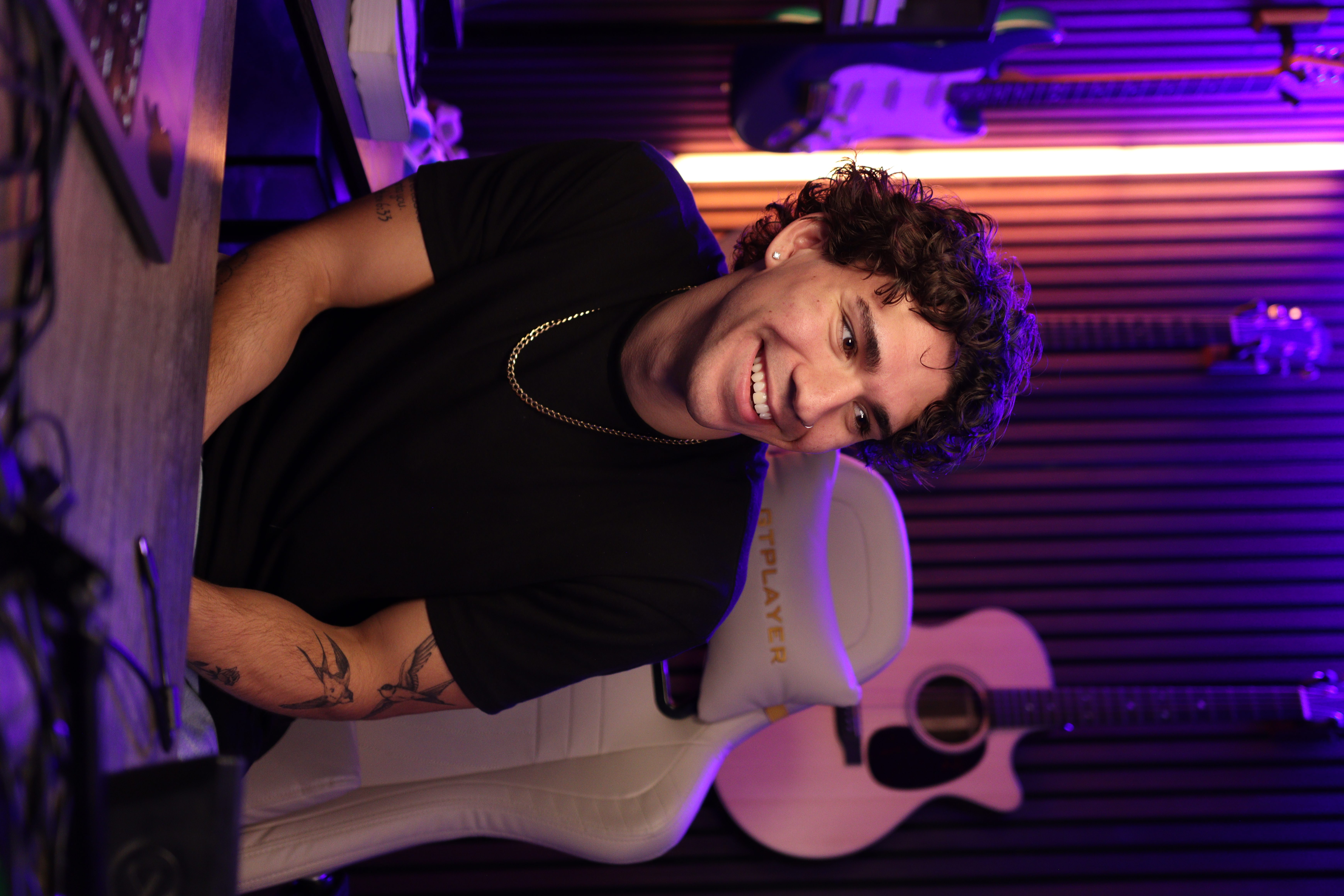 Cam smiling in his studio, with guitars hanging behind him