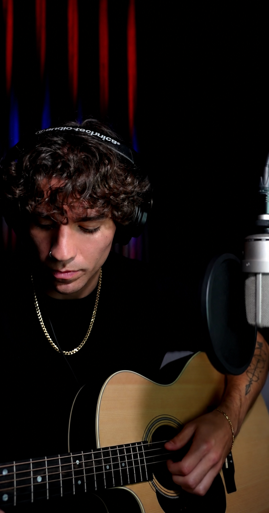 Cam Carroll playing acoustic guitar beside a studio microphone